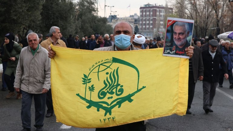 An protester holds the flag of the Afghan Shiite group Liwa Fatemiyoun, a militia formed in 2014 to fight in Syria on the side of the regim, during a protest in support of Yemen and Palestinians, following the Friday noon prayers in Tehran on January 12, 2024, amid continuing battles between Israel and Hamas in Gaza. Portrait (R) shows top Iranian general Qasem Soleimani, who headed the Islamic Revolutionary Guard Corps